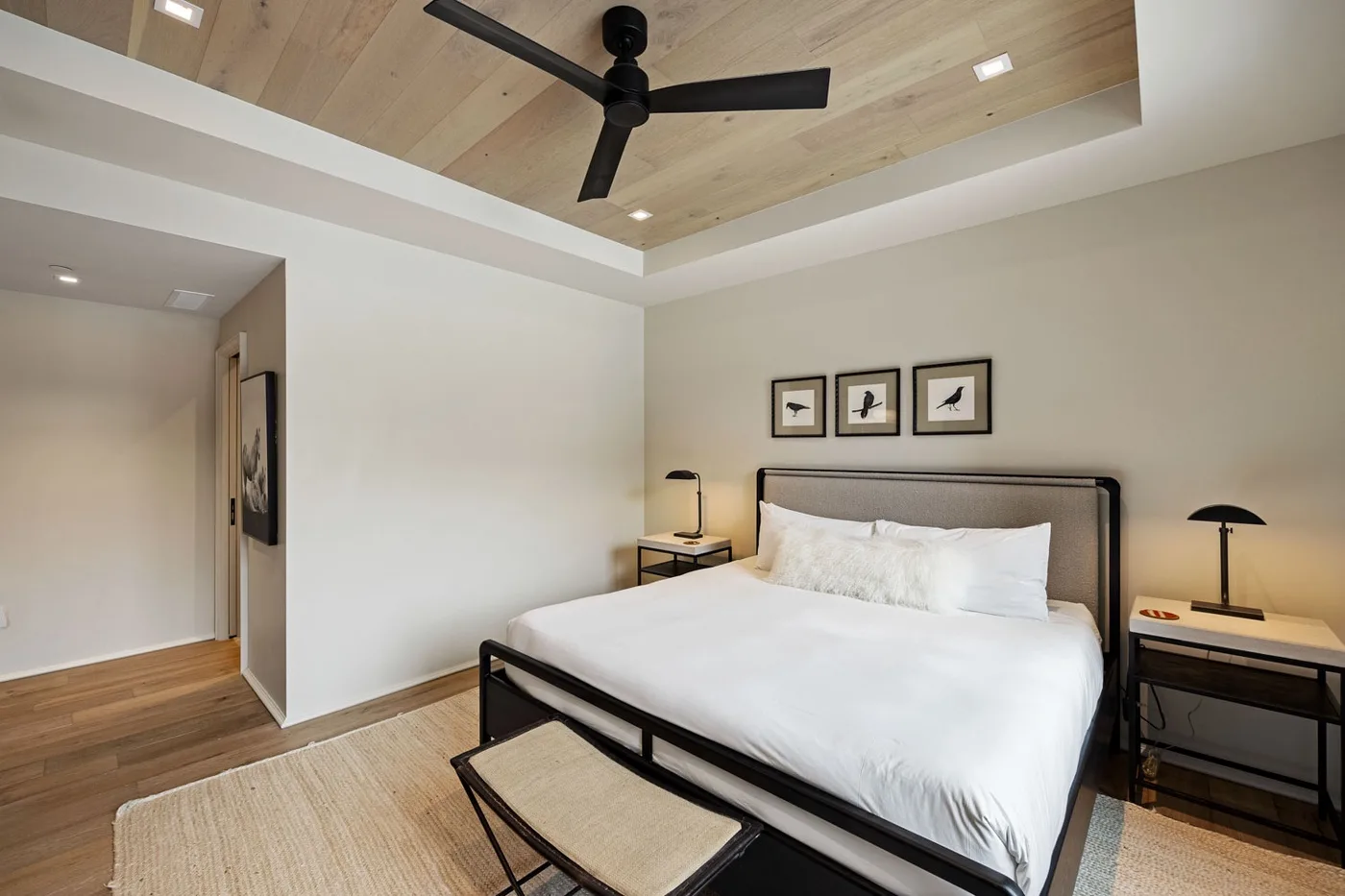 A bedroom with a bed, framed artwork, and a ceiling fan.
