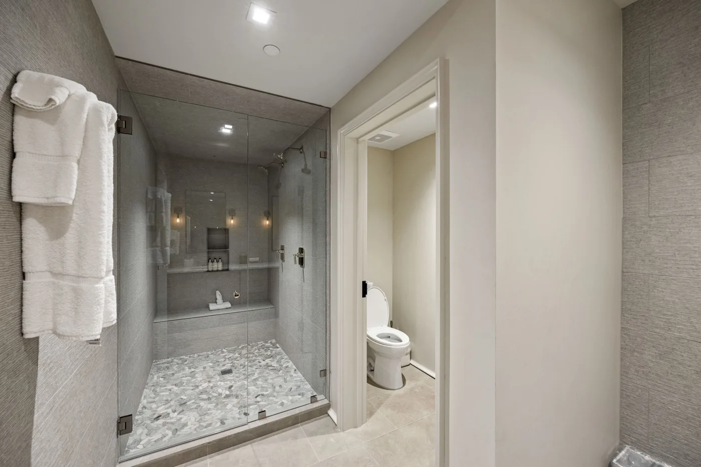 A modern bathroom with a glass shower and an adjacent toilet.