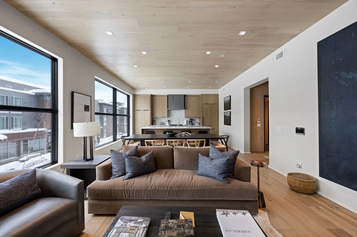 A modern living room opens onto a dining area and kitchen, with large windows.