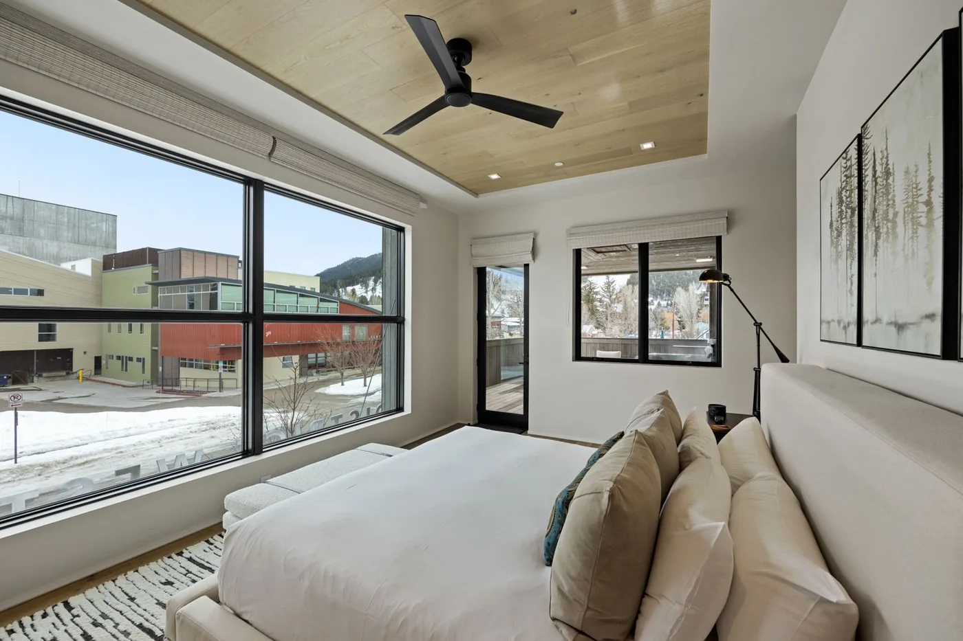 A bright bedroom with a large bed, broad windows, and a ceiling fan.