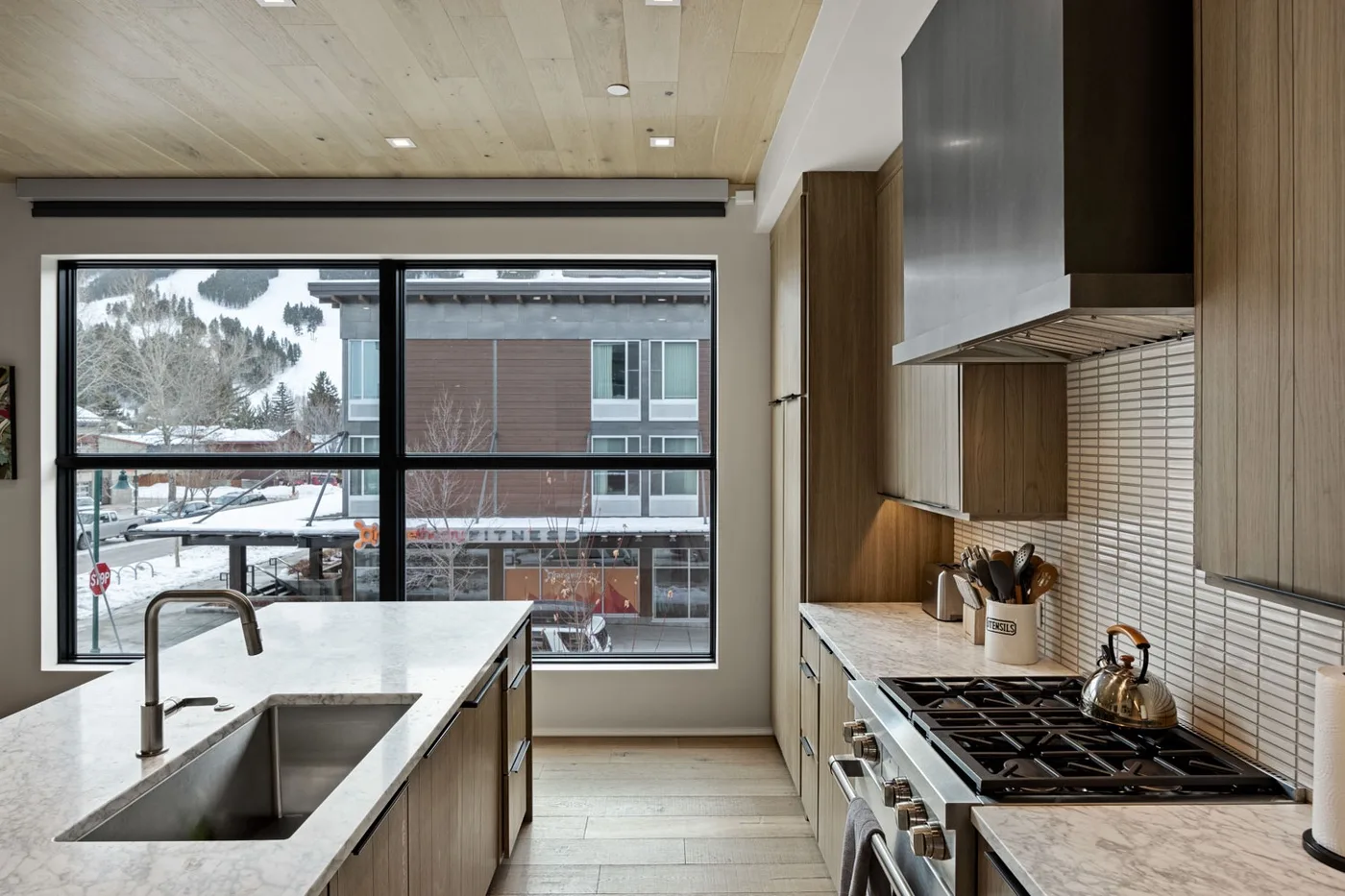A modern kitchen with a large island, sink, and broad windows.