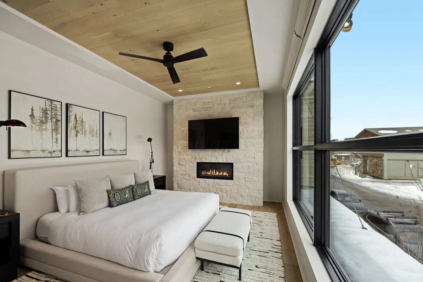 A bedroom with a large bed, wall-mounted television, and tall windows.