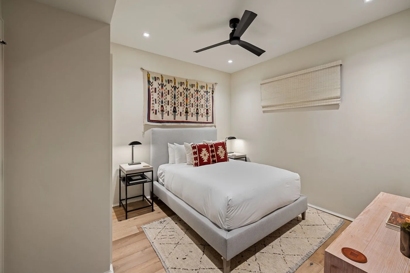A bedroom with a white bed beneath a patterned wall hanging.