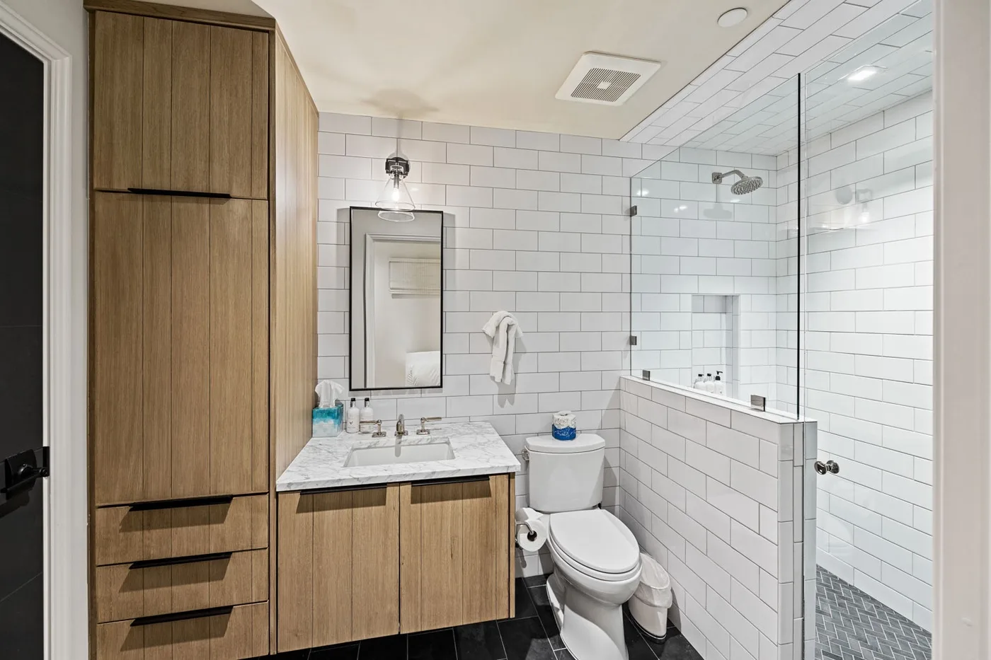 A bathroom with a tiled shower, vanity, and toilet.
