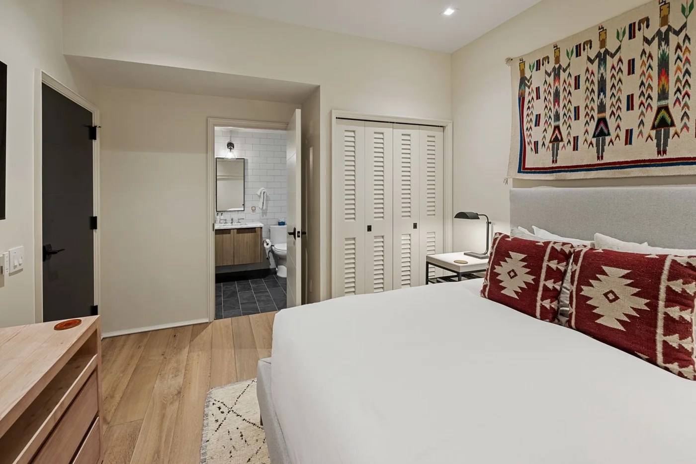 A bedroom with a neatly made bed and a bathroom visible through the doorway.