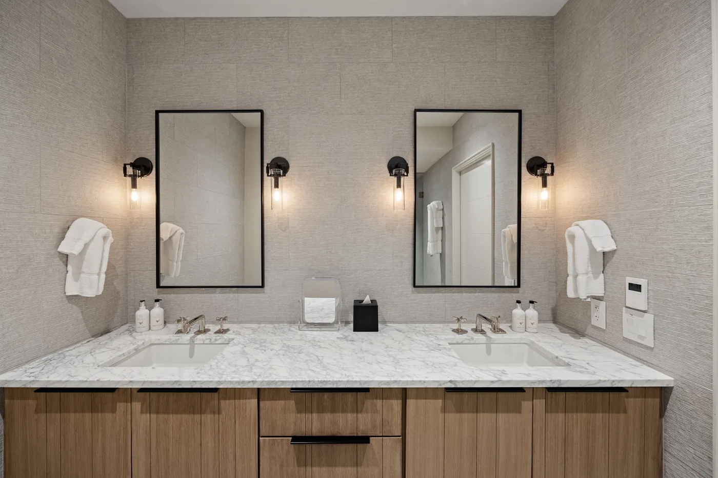 A bright bathroom vanity with two sinks, mirrors, and warm wall lights.