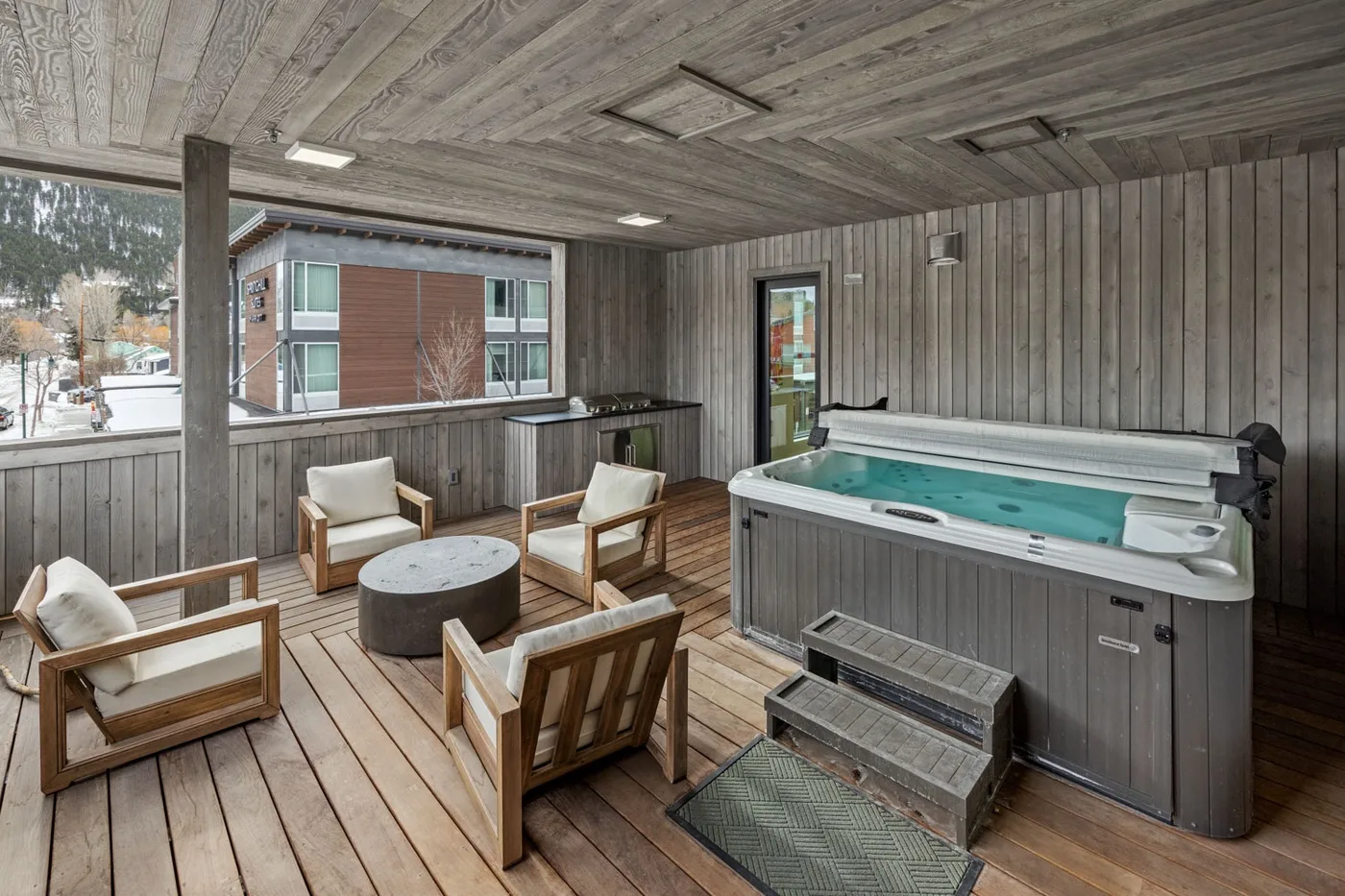 A covered wooden deck has a hot tub and a small seating area.