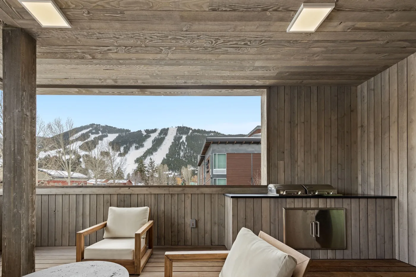A wood-paneled lounge with seating overlooks a snowy mountain landscape.