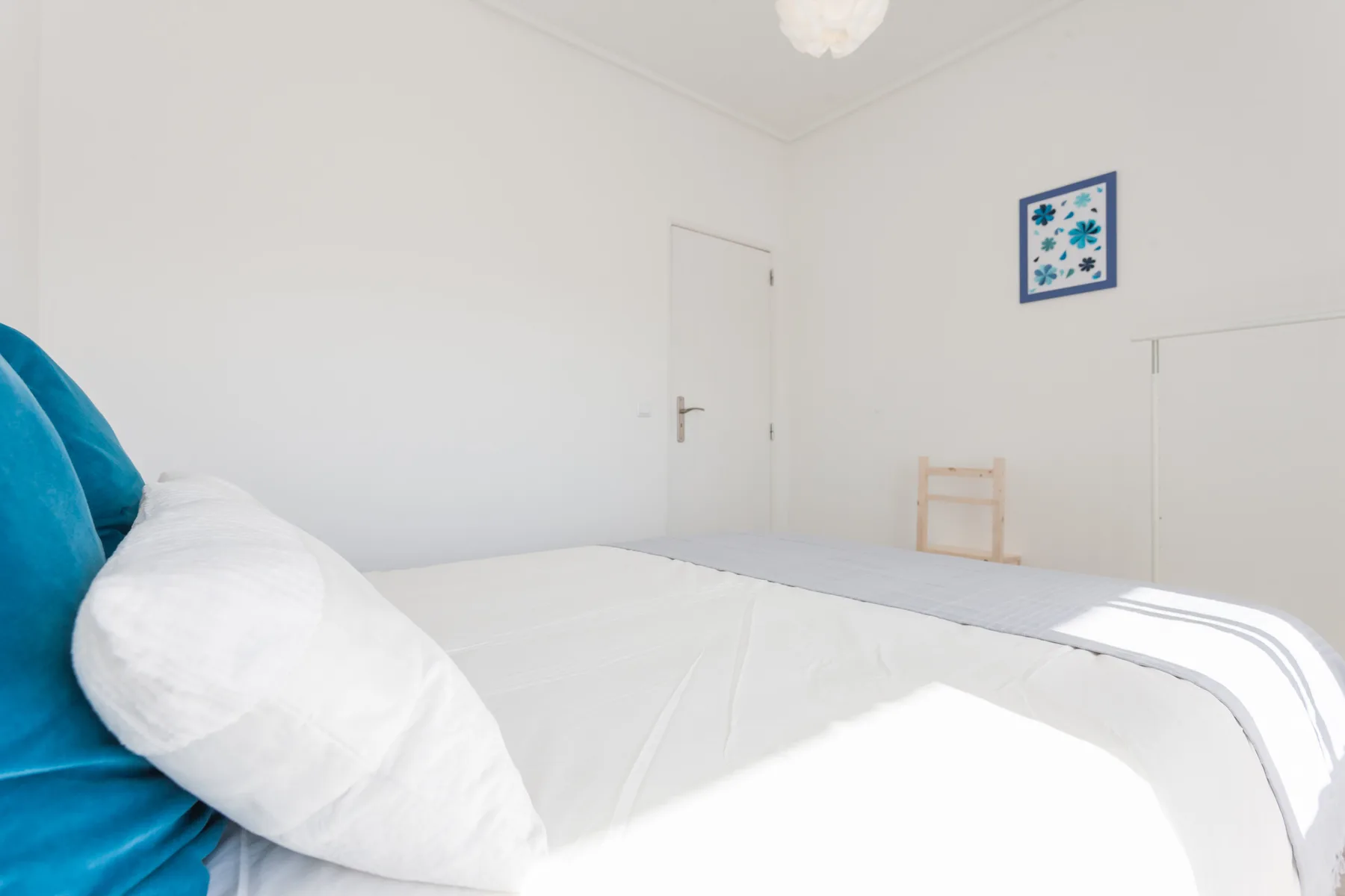 Un dormitorio luminoso con ropa de cama blanca y un cabecero tapizado azul.