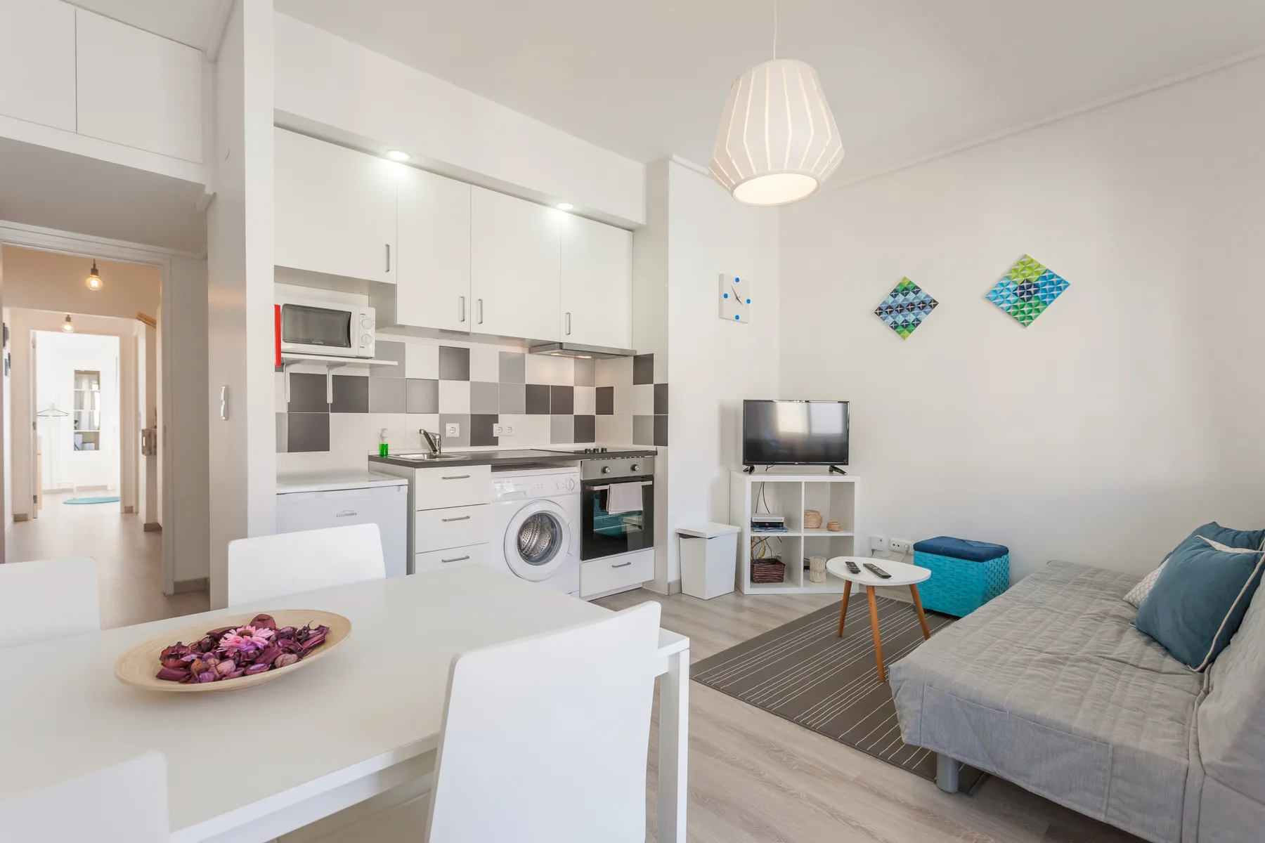 Una luminosa sala de estar diáfana con mesa de comedor, cocina pequeña y sofá.