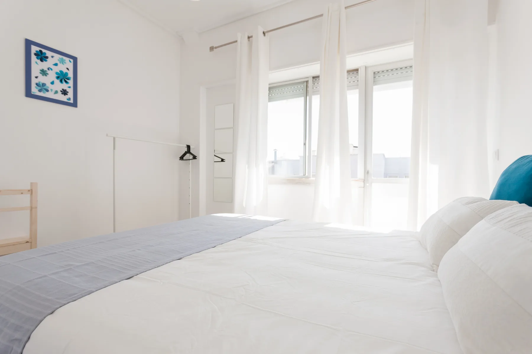 Un dormitorio luminoso con una cama junto a ventanas altas.