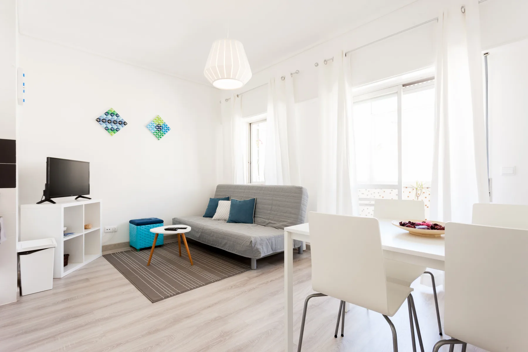 Una sala de estar luminosa con sofá gris, televisor y mesa de comedor.