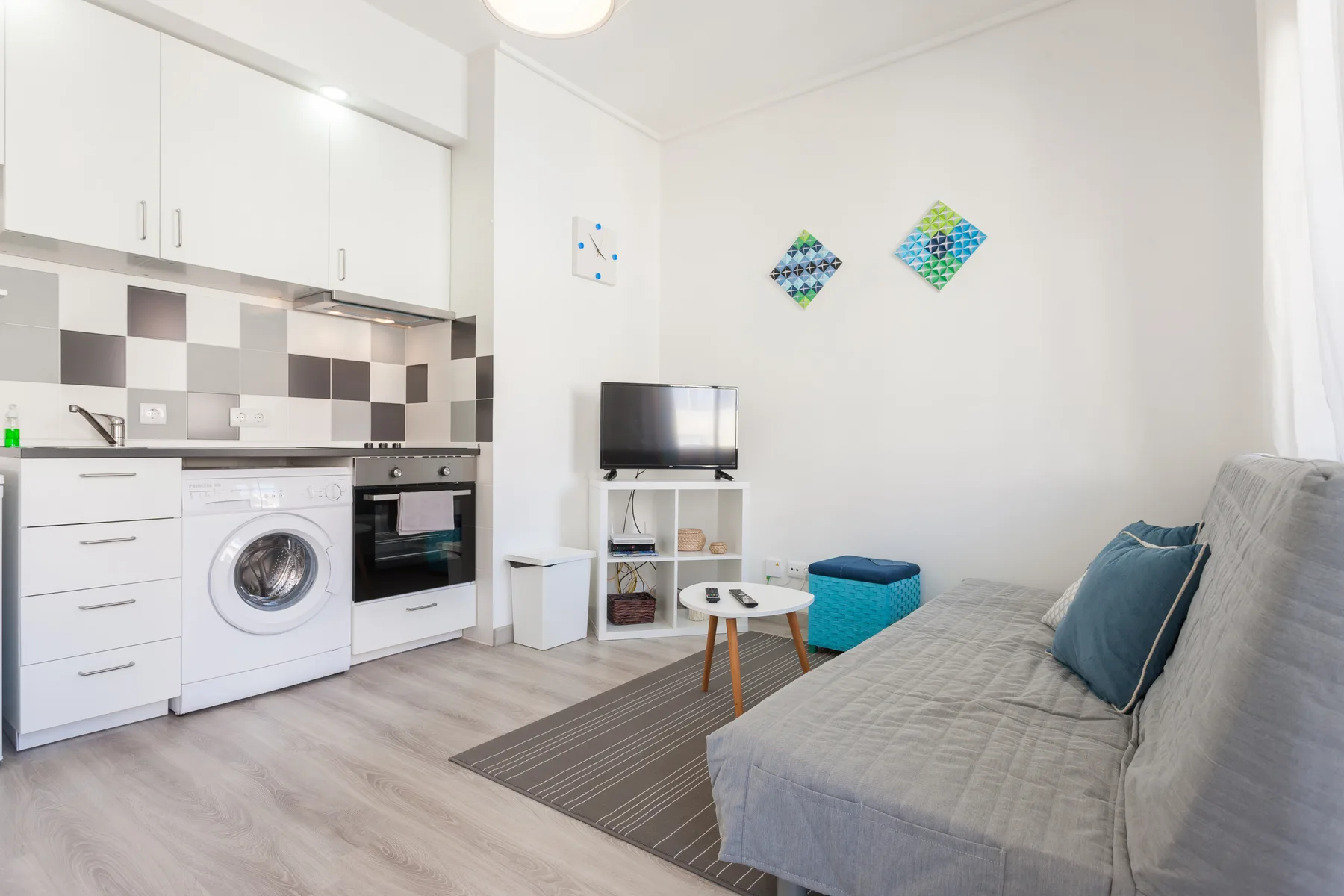 Una luminosa sala de estar tipo estudio con cocina compacta, televisión y asientos.
