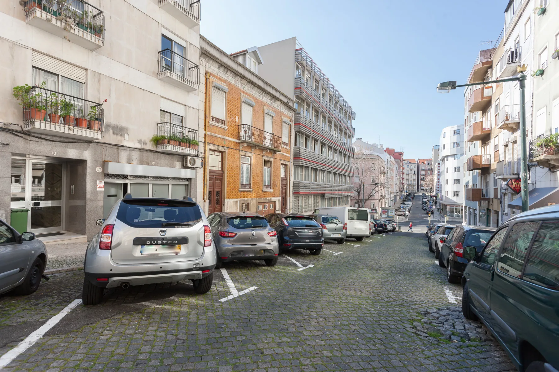 Una calle urbana empedrada, flanqueada por coches aparcados y edificios de apartamentos.
