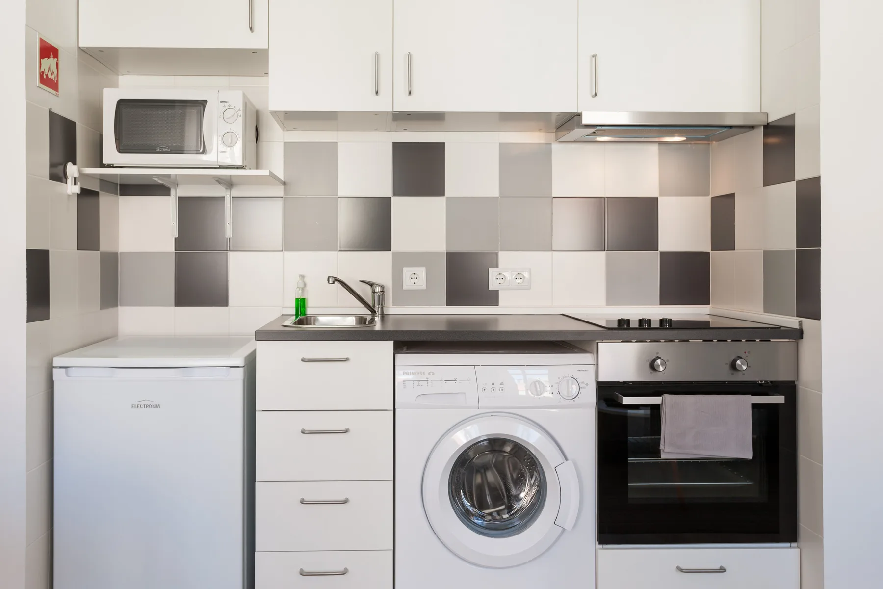 Una cocina compacta con armarios blancos, una lavadora y un horno.