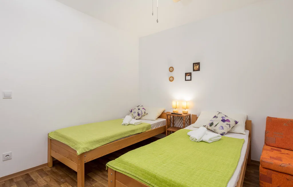 A bright bedroom with two beds dressed in green and a bedside table.