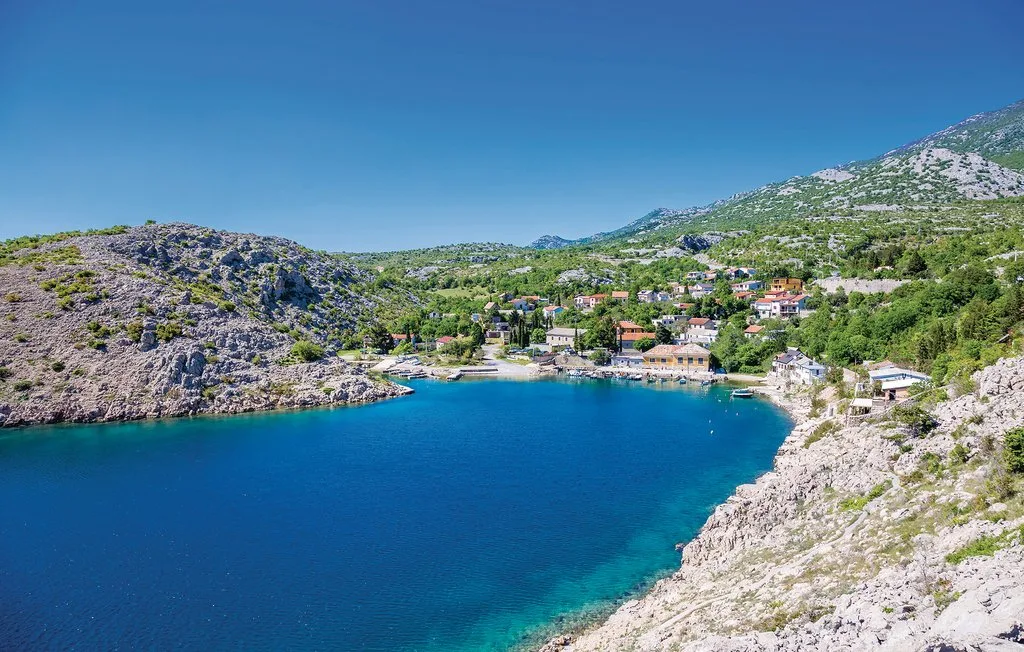 A blue coastal bay sits below green hills dotted with buildings.