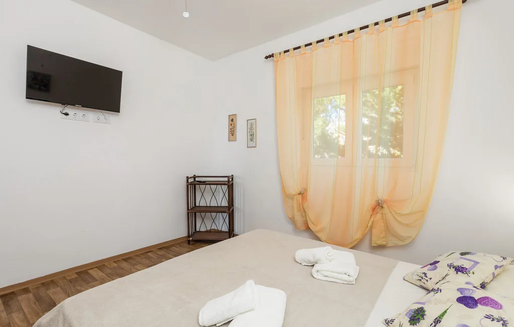 Un dormitorio con una cama, toallas dobladas y una ventana luminosa con cortinas transparentes.