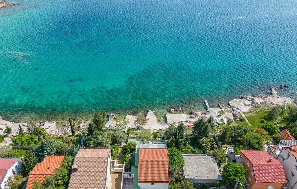 An aerial view of homes along a rocky shoreline beside clear turquoise water.