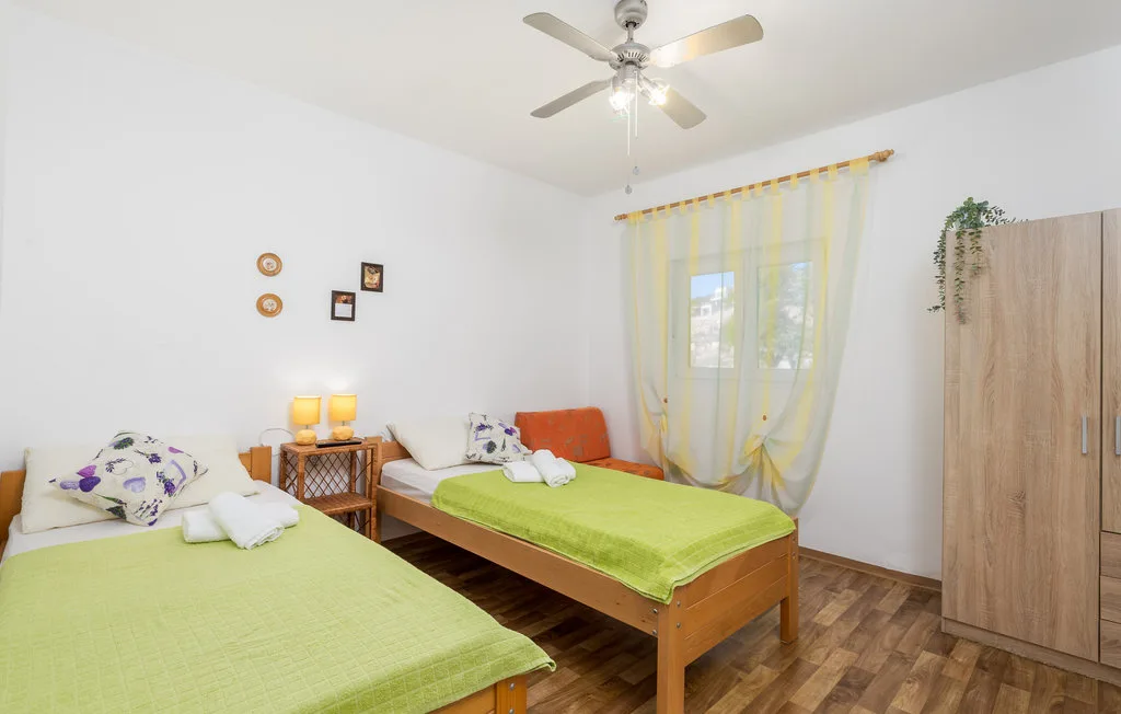 A bright bedroom with two beds covered in green bedspreads and a curtained window.