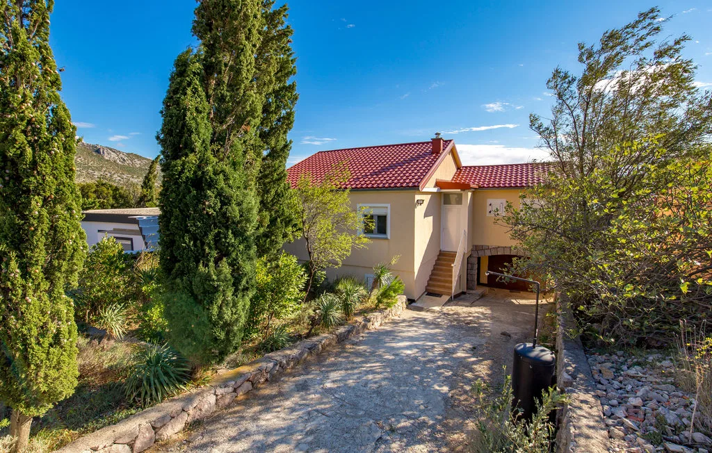 Una casa con techo de tejas rojas está junto a un camino de grava bordeado de árboles.