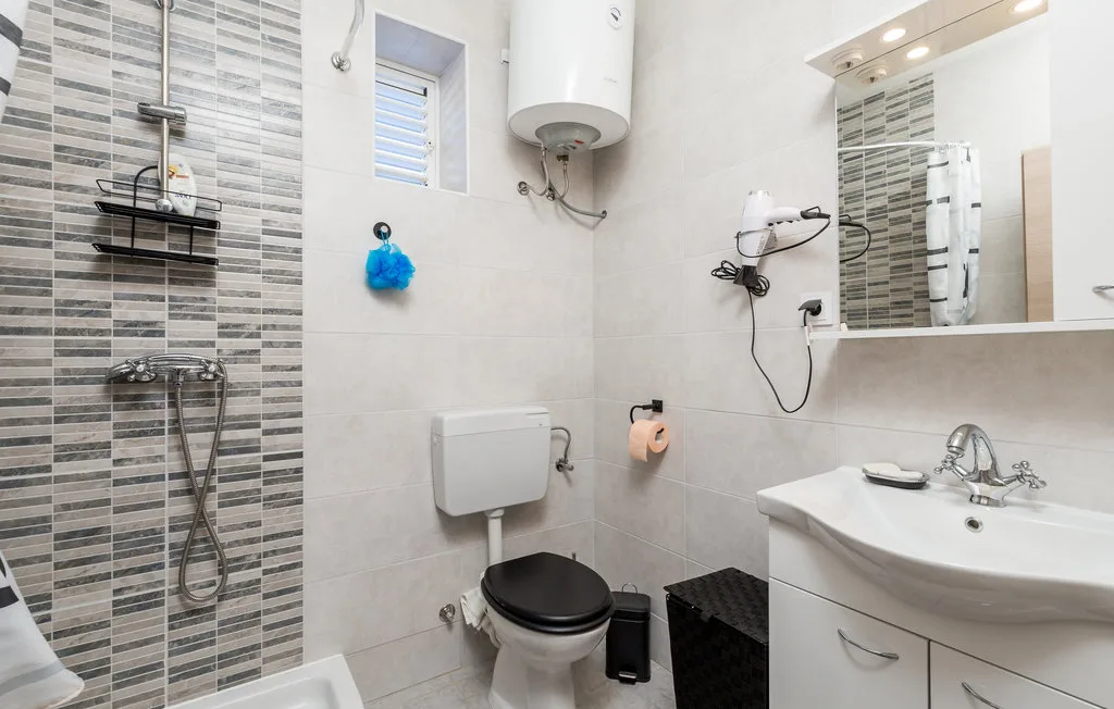A tiled bathroom with a shower, toilet, and sink beneath a mirror.