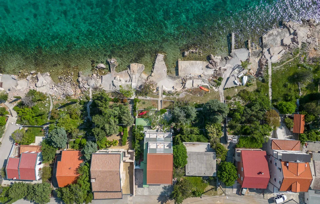 Aerial view of a coastal shoreline with clear water, rocky ground, and nearby buildings.