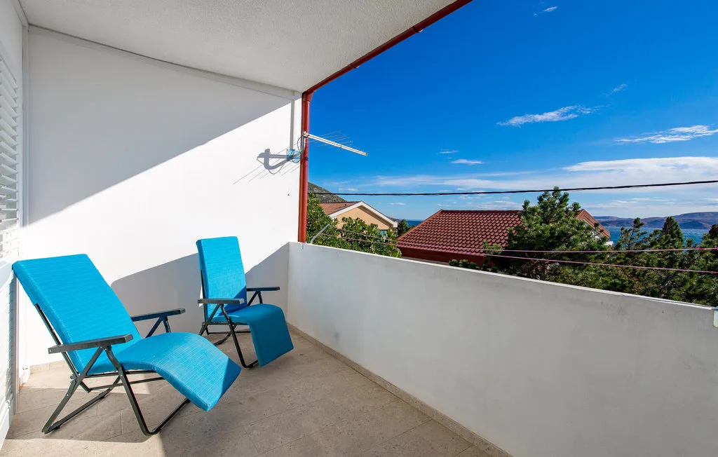 A balcony with blue seating overlooks rooftops and a distant sea.
