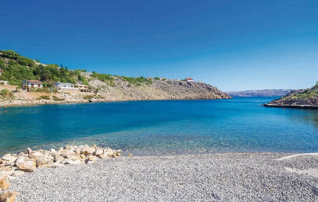 A rocky shoreline borders clear blue water beneath a bright, open sky.