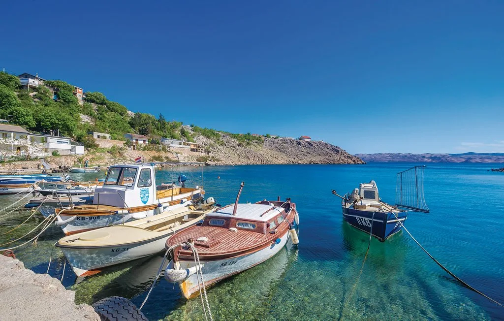 Small boats are moored in clear water beside a rocky shoreline.