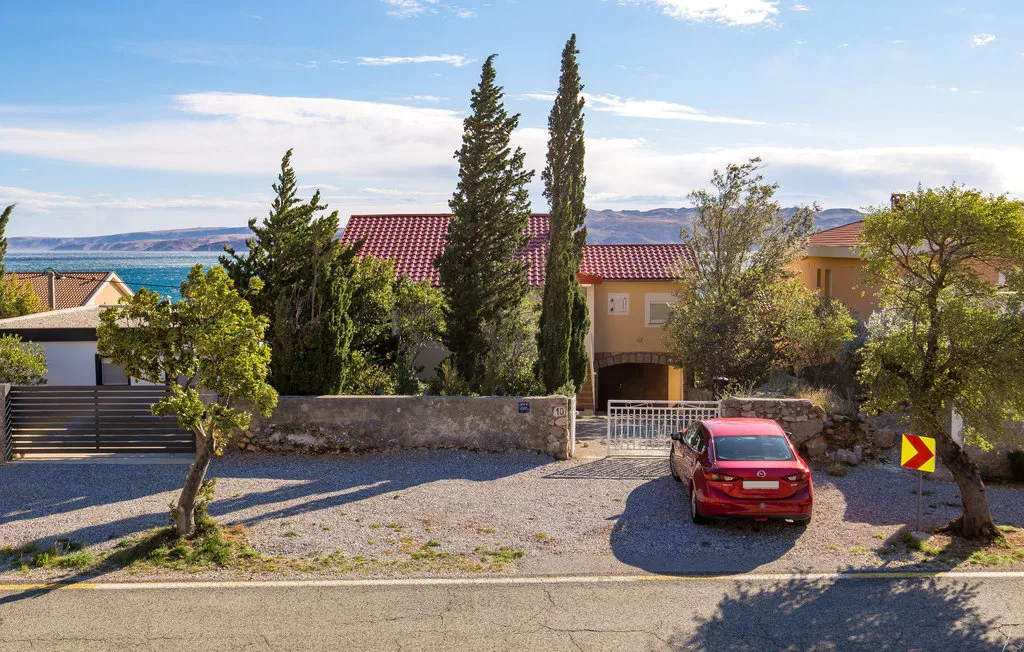 A red car is parked in a gravel driveway beside a low stone wall.