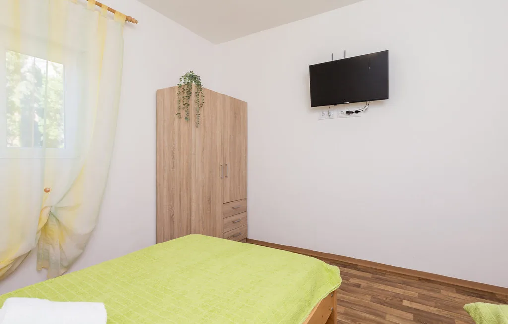 A bedroom with a bed covered in a bright green bedspread and a wall-mounted television.