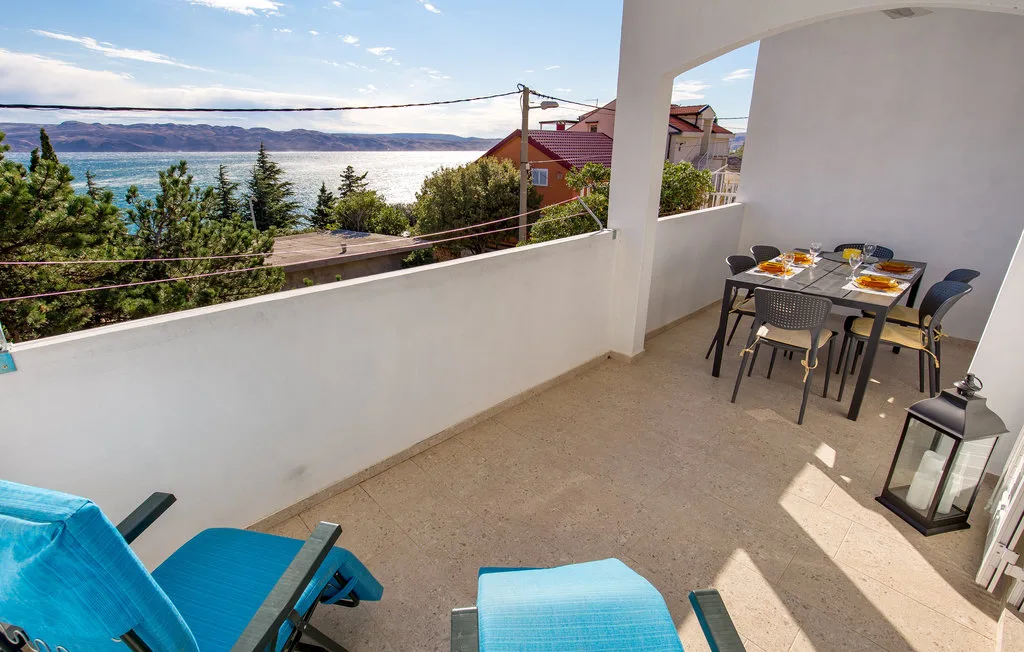 A sunny balcony has blue lounge seating and a dining table overlooking the water.