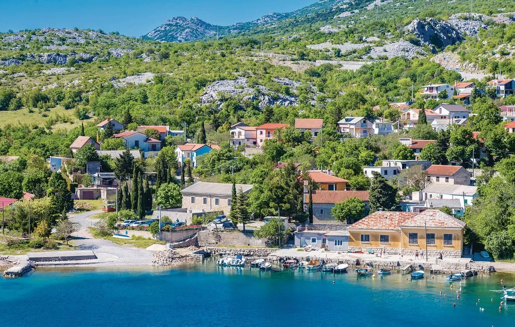 A coastal village of hillside homes overlooks a clear blue bay.