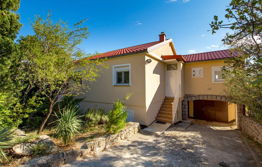 A stucco house with a red tiled roof stands beside a stone garden wall.