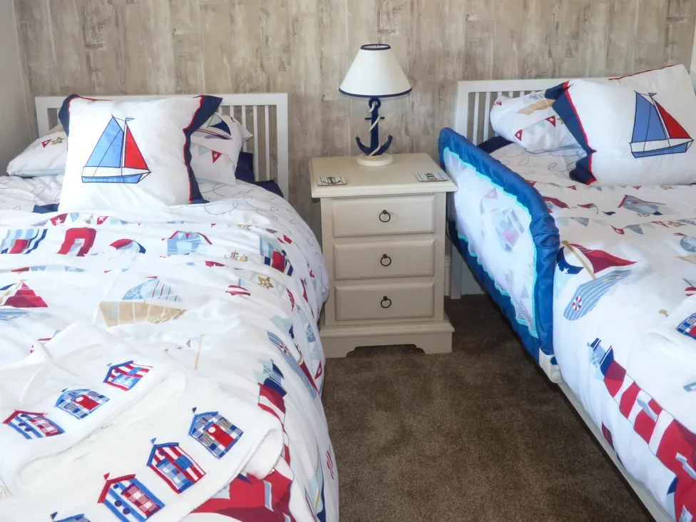 A bedroom with two single beds with nautical themed bedding and a bedside table with a lamp at Lockton Cottage in Pickering