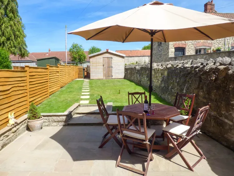 An outdoor patio with a wooden dining set beneath a large umbrella.