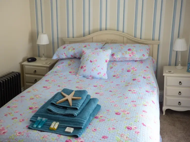 A bedroom with a floral bedspread and folded teal towels on the bed.