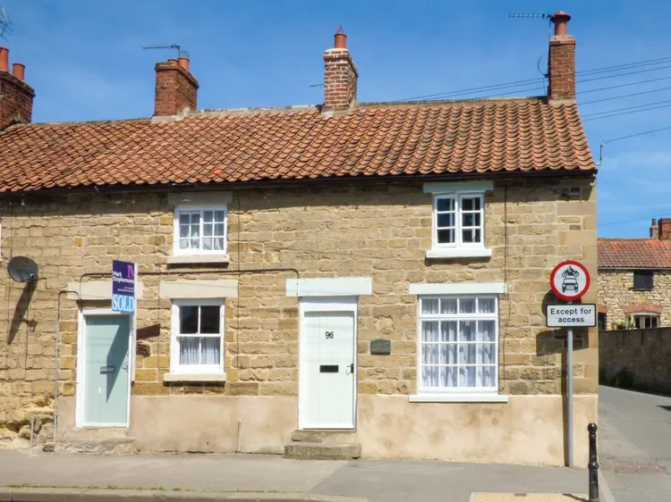 A stone building with a tiled roof and white-framed windows along a street.