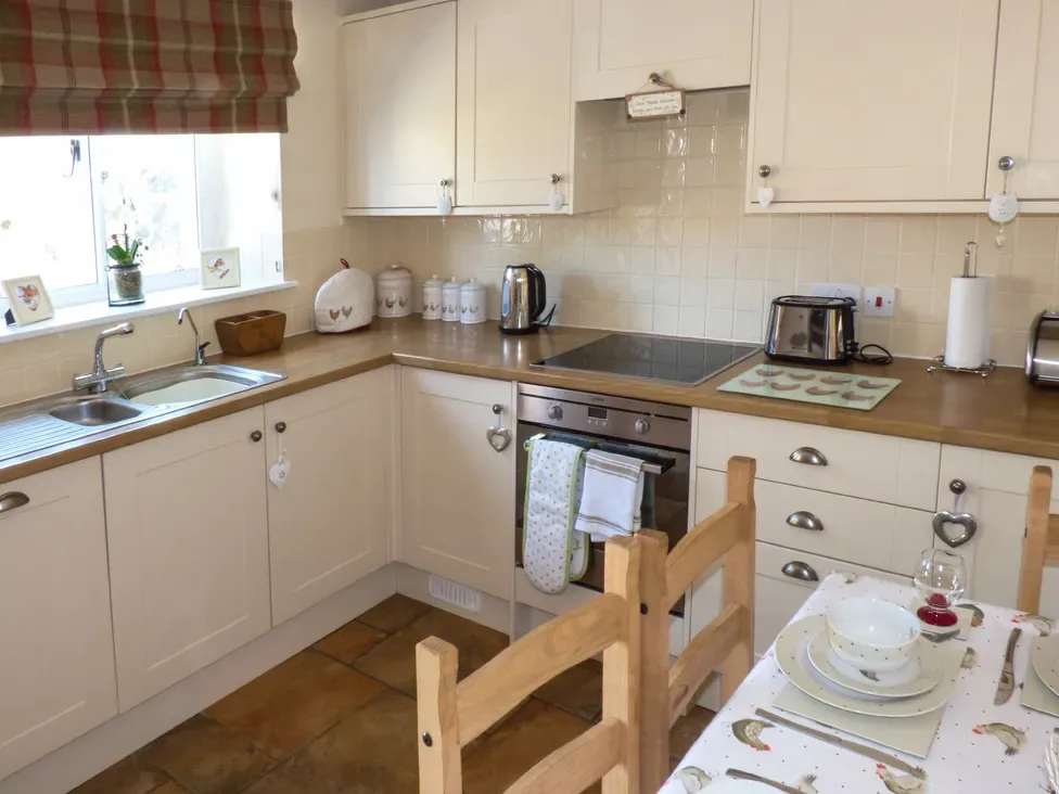 A bright kitchen with white cabinets, wooden countertops, and a dining table set with dishes.