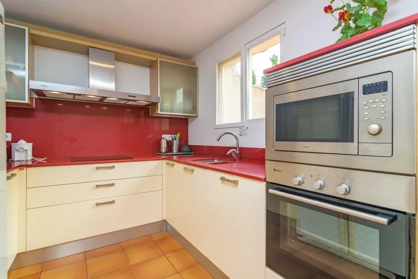 A kitchen with cream cabinets, red countertops, and built-in cooking appliances.