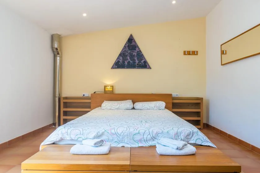 A bedroom with a double bed, wooden bedside shelving, and a triangular wall decoration.