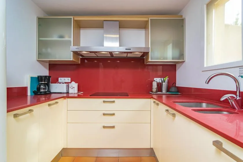 A bright kitchen with cream cabinets, red countertops, and a stainless steel range hood.