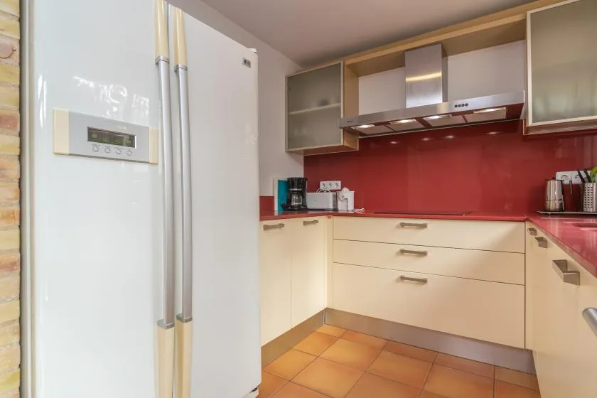 A modern kitchen with pale cabinets, a red backsplash, and a large refrigerator.