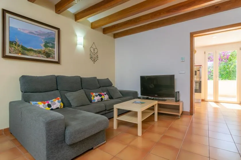 A living room with a sectional sofa, television, and exposed wooden ceiling beams.