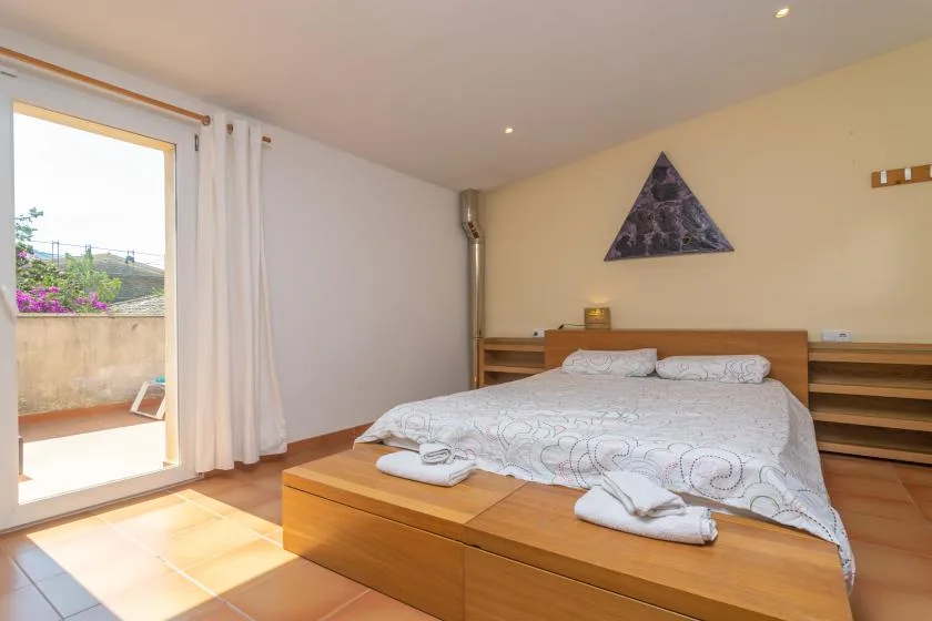 A bedroom with a bed, wooden headboard, and sliding glass door opening to a terrace.