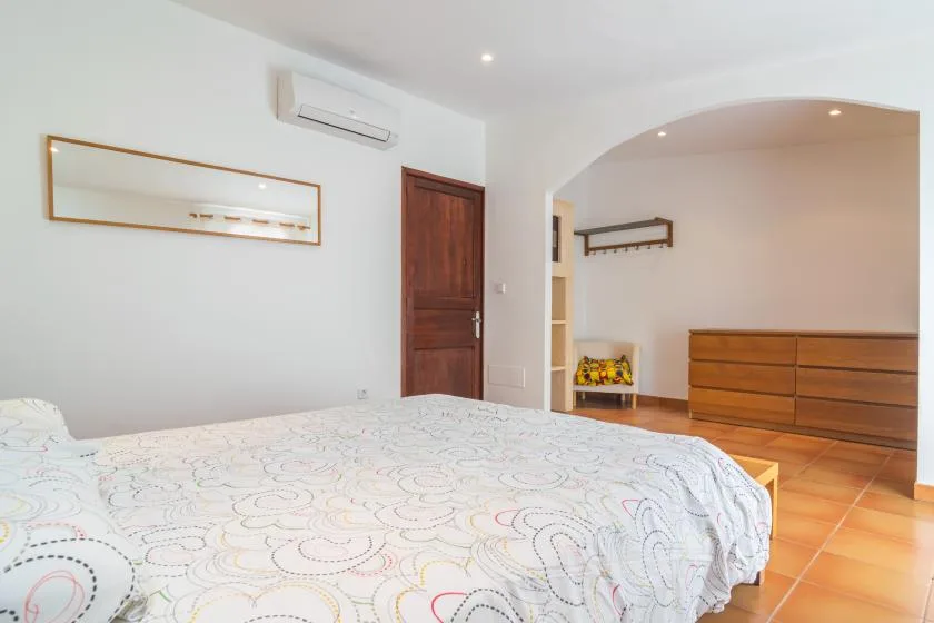 A bedroom with a patterned bedspread and wooden dresser.