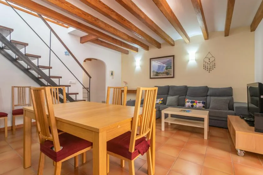 A dining and living area with a wooden table, seating, and exposed ceiling beams.