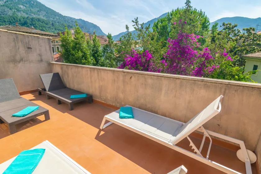 A sunlit terrace with lounge seating overlooks flowering trees and green hills.