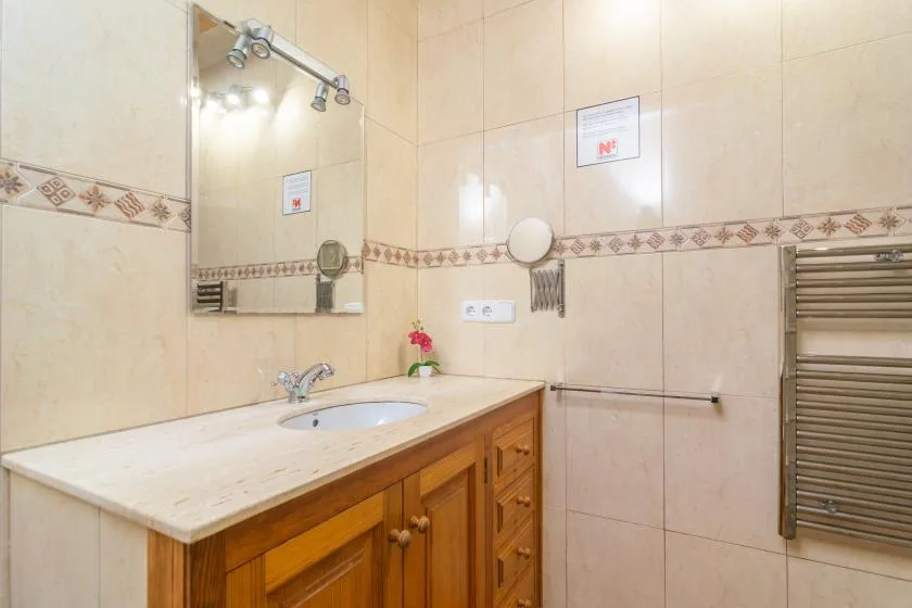 A tiled bathroom vanity with a sink, wooden cabinetry, and a wall-mounted towel rail.
